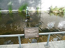 Bronze statue of a smiling cherub holding a fish Morris Singer bronze of boy with a fish at Enfield Civic Centre 02.jpg