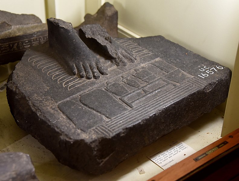File:Part of base of basalt royal statue. Queen's feet on 9 bows before an offering table. Hotep sign at front edge. Hes vase with spouted vases and lamp. Late Period. From Egypt. The Petrie Museum of Egyptian Archaeology, London.jpg