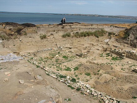 The remains of the wall of a small structure are seen in the foreground, the Sea of Azov is visible in the background.