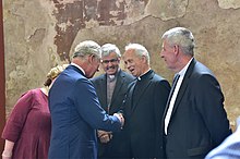 Fr Eugene O'Hagan shaking hands with the Prince of Wales. Also pictured are Protestant clergy Stephen Forde and Charles McMullen Prince of Wales and Duchess of Cornwall visit to Northern Ireland, June 2018 (40944623630).jpg