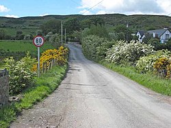 Un punto di attraversamento senza demarcazione visibile, visto dall'Irlanda del Nord, con passaggio nello Stato d'Irlanda indicato dal segnale del limite di velocità km/h.