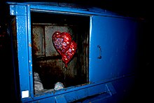 A wrapped, unopened Valentines Day gift with heart-shaped helium balloons attached sits discarded in a dumpster. Unhappy Valentine.jpg