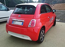 Rear quarter view Fiat 500e in Arancio Electrico Perla (electric orange), showing hatch-mounted rear spoiler