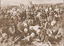 Photograph of a large number of soldiers reading from pieces of paper