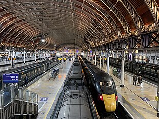 A long, green GWR train in the platform beneath London Paddington's large, arch roof.