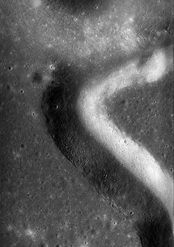 A section of a panoromic camera photograph showing a high resolution view of the landing site. Boulders are easily seen in the rille and the ground disturbed by the lunar module engine shows as a white patch at lower left. South is up. Apollo 15 panaromic camera landing site.jpg