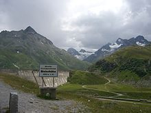 Hinweisschild auf der Bielerhöhe, von Westen kommend, mit der Staumauer, die den alten Talgrund der Vermunter Passhöhe überspannt (der eigentliche Pass war am östlichen Damm)