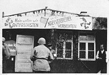 Anti-nazi banner outside a barrack at Buchenwald. The sign, in rhyme, says "We anti-fascists want to go home to eradicate Nazi criminals". Buchenwald Anti-Nazi Banner 73316.jpg