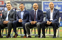 Andy Pettitte, Jorge Posada, Mariano Rivera et Derek Jeter vêtus de costumes et assis sur des chaises sur un terrain de baseball.