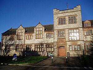 Part of a stone building seen from the front. Towards the right of the picture is a three-storey square tower containing a door. The building extends on both sides of the tower and has two storeys; the portion of the building to the left contains two gables.