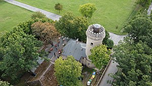 Rückansicht des Ferberturms mit angeschlossenem Restaurantgebäude aus der Vogelperspektive; umgeben von Bäumen und einer Wiese.