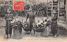 Trois petites filles asiatiques d'une dizaine d'années, en habit traditionnel, portant des grands paniers remplis de fleurs.