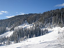 Foto van een besneeuwde berg met schansspringheuvels.