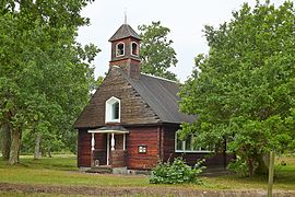 Een houten kapel midden in een weiland met enkele bomen.