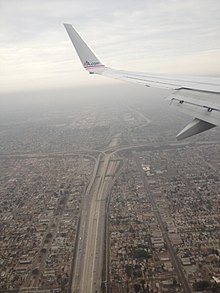 Vemos el ala de un avión en la parte superior de la imagen, el intercambio en la parte inferior con casas a ambos lados.