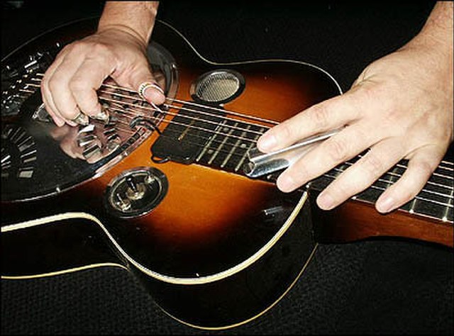 Wooden resonator guitar played with a steel, angled to form a chord unavailable from straight open tuning