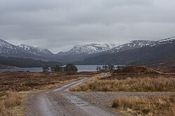 Tog'lar bilan o'ralgan ko'lga olib boradigan, qurilmagan yo'l