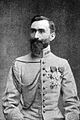 Foto de un hombre con uniforme militar, sentado, con la cabeza descubierta y barba.