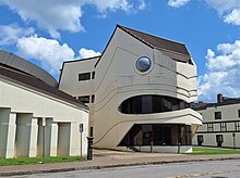 A three story building shaped like a turtle's head. The building has been painted white and is boarded up.