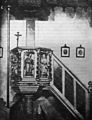 Černobílá fotografie kazatelny z roku 1916, kde je viditelná ferula a původní kříž ze svatostánku, který stojí na kazatelně, na zdi jsou viditelné obrázky pašijí