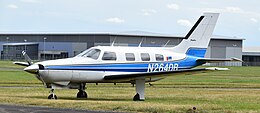 A white and blue light aircraft parked on a grassy airfield