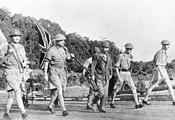 ארתור פרסיבל צועד בעקבות קצין יפני, ותחת דגל לבן, על מנת לשאת ולתת עם היפנים בנוגע לתנאי הכניעה של כוחותיו.