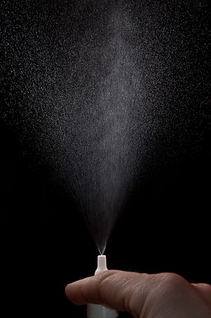 A hand sprays a mist of nasal spray from a pump.