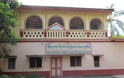 A two-storey pink-and-yellow building with a sign in Bengali and English