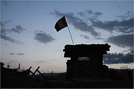 Uma bandeira voa acima de uma torre militar contra um céu escuro.