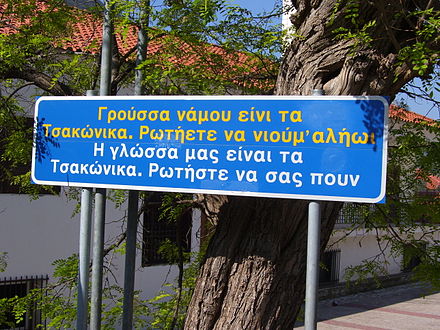 (Tsakonian/Greek) "Our language is Tsakonian. Ask and they'll tell you". Greek sign in the town of Leonidio.