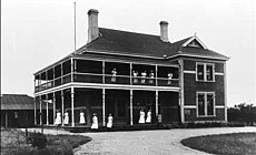 A large Federation style brick building with verandas and balconies, on which a dozen women in white are standing.