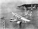 Pan American Airways Sikorsky S-42 "Pan American Clipper" em vôo sobre a ponte em construção San Francisco-Oakland Bay.jpg