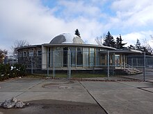 The Queen Elizabeth Planetarium in October 2016. The building is surrounded by a wire fence due to its dilapidation. Queen Elizabeth Planetarium Edmonton 2016.jpg