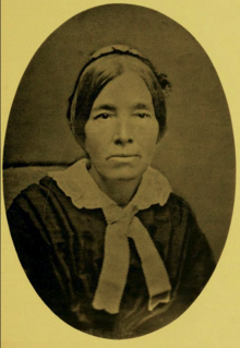 B&W oval portrait photo of a middle-aged woman with her hair in an up-do, wearing a dark shirt with a white collar.