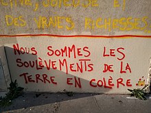 Texte peint en rouge sur un mur en majuscules, "Nous sommes les Soulèvements de la Terre".
