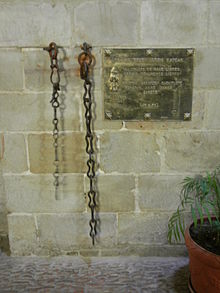 Photographie de deux chaînes pendantes d'un mur à côté d'une plaque de laiton brillant.