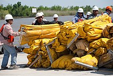 Men in hard hats standing near water next to large pile of bundled large yellow deflated rubber tubing