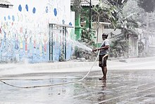 A man holding a hose and spraying volcanic ash with water