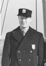 Czarno-białe zdjęcie przedstawiające mężczyznę w czapce i płaszczu.