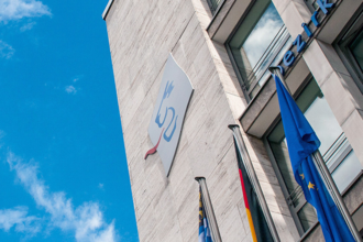 Ein helles Gebäude mit dem Logo des Bezirks Oberbayern und einer blauen Fahne am Gebäude