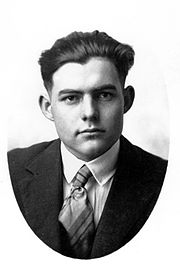 Hemingway à 18 ans, de face, vêtu d'une veste sombre et d'une cravate rayée, portée sur une chemise blanche.