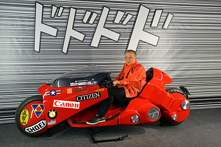 Otomo posing on a replica of a futuristic motorcycle seen in his series Akira (2016)
