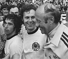 Beckenbauer (al centro) festeggia la vittoria del Mondiale 1974 con Gerd Müller (a sinistra) ed Helmut Schön (a destra).