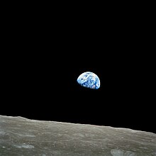 El petit semicercle blau-blanc de la Terra, gairebé que brilla intensament amb el color a la negror de l'espai, s'aixeca sobre la desolació, el cràter de la superfície de la Lluna.