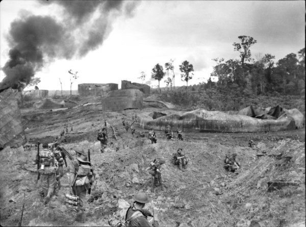 Australian infantry advancing through wrecked oil storage tanks at Tank Hill, Tarakan.
