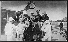 Former U.S. President Theodore Roosevelt (seated, at left) and friends mount the observation platform of a Uganda Railway locomotive Uganda Railways - Theodore Roosevelt.jpg