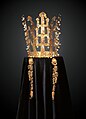 Couronne faite de bandeaux en or en forme d'arbres dressés aux feuilles d'or et pendentifs de jade (en forme de virgule). Photographie de face, sur fond sombre, la couronne étant posée sur un velours noir.