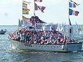 Vue du bateau de pêche The Breau's II au port de Caraquet, durant la bénédiction des bateaux. Il est décoré du drapeau du Nouveau-Brunswick, du drapeau du Canada, du drapeau de l'Acadie et de guirlandes de fanions bleus, blancs et rouges.