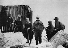 Photo anienne d'une petite cabane de bois située derrière un groupe de huit personnes chaudement couvertes, avec des rochers au premier plan.