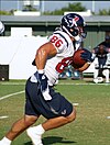 An football player running from left to right on a football field. He is wearing a red, blue and white uniform